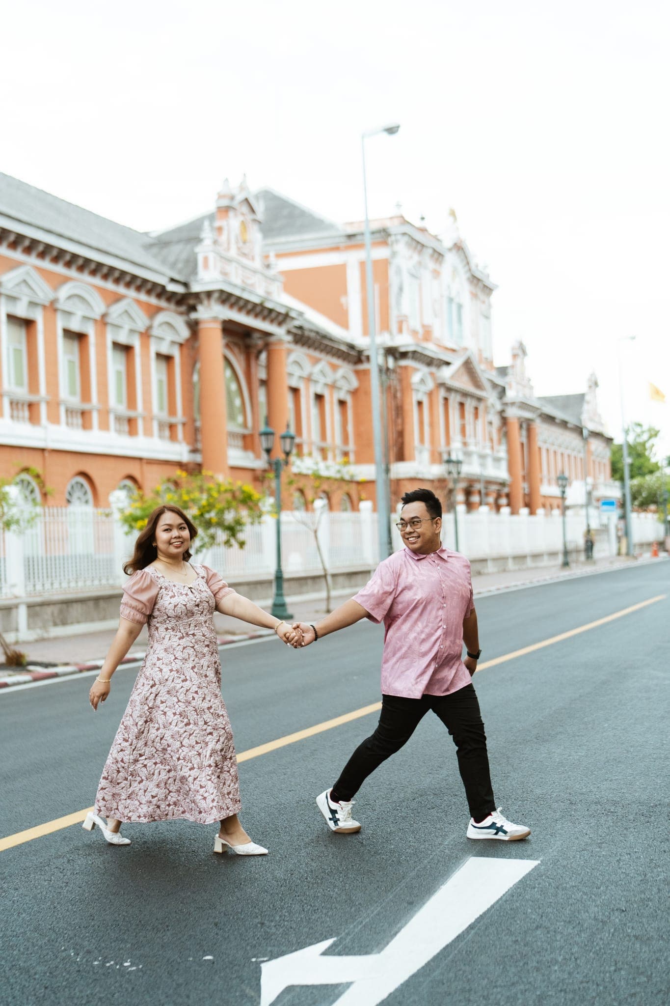 Sam and Angela walking hand in hand across a street in front of an ornate red-and-white building