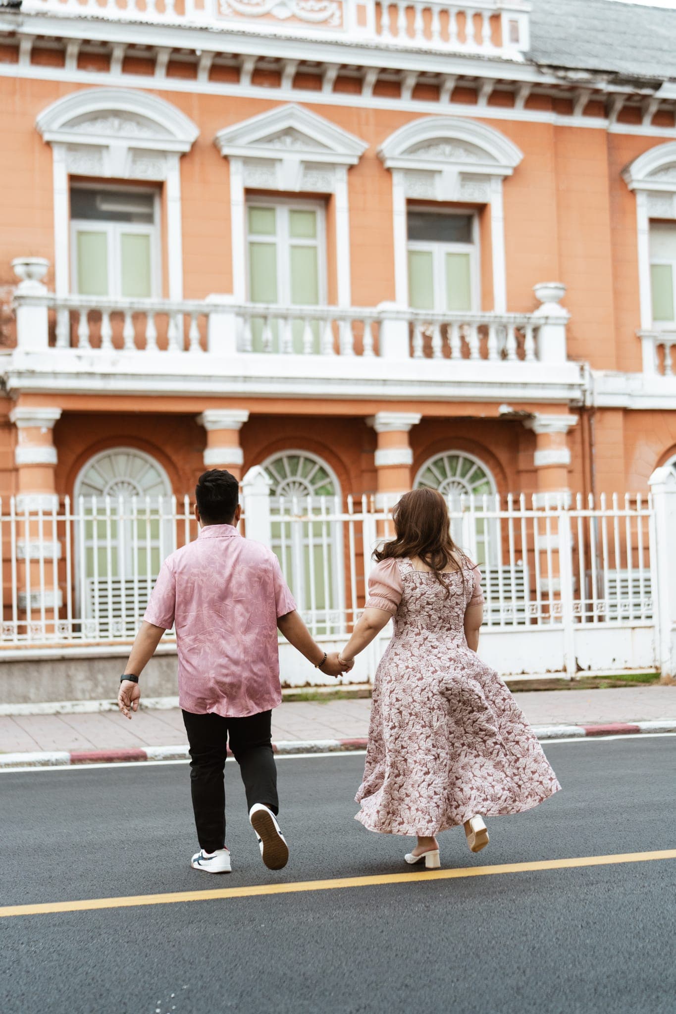 Sam and Angela walking hand in hand toward the arched gates of the red-and-white building