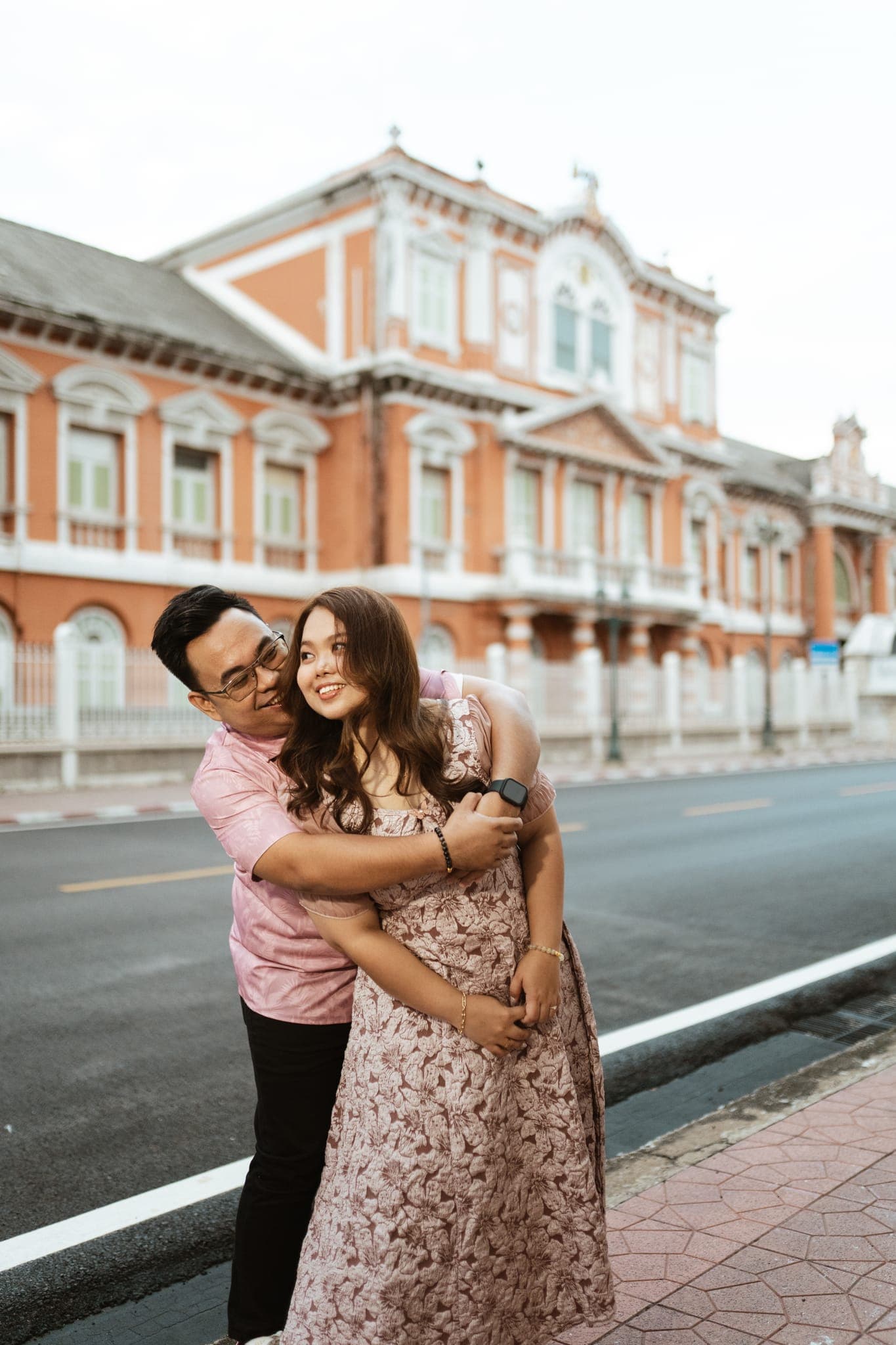 Sam hugging Angela from behind on the street outside the red-and-white building