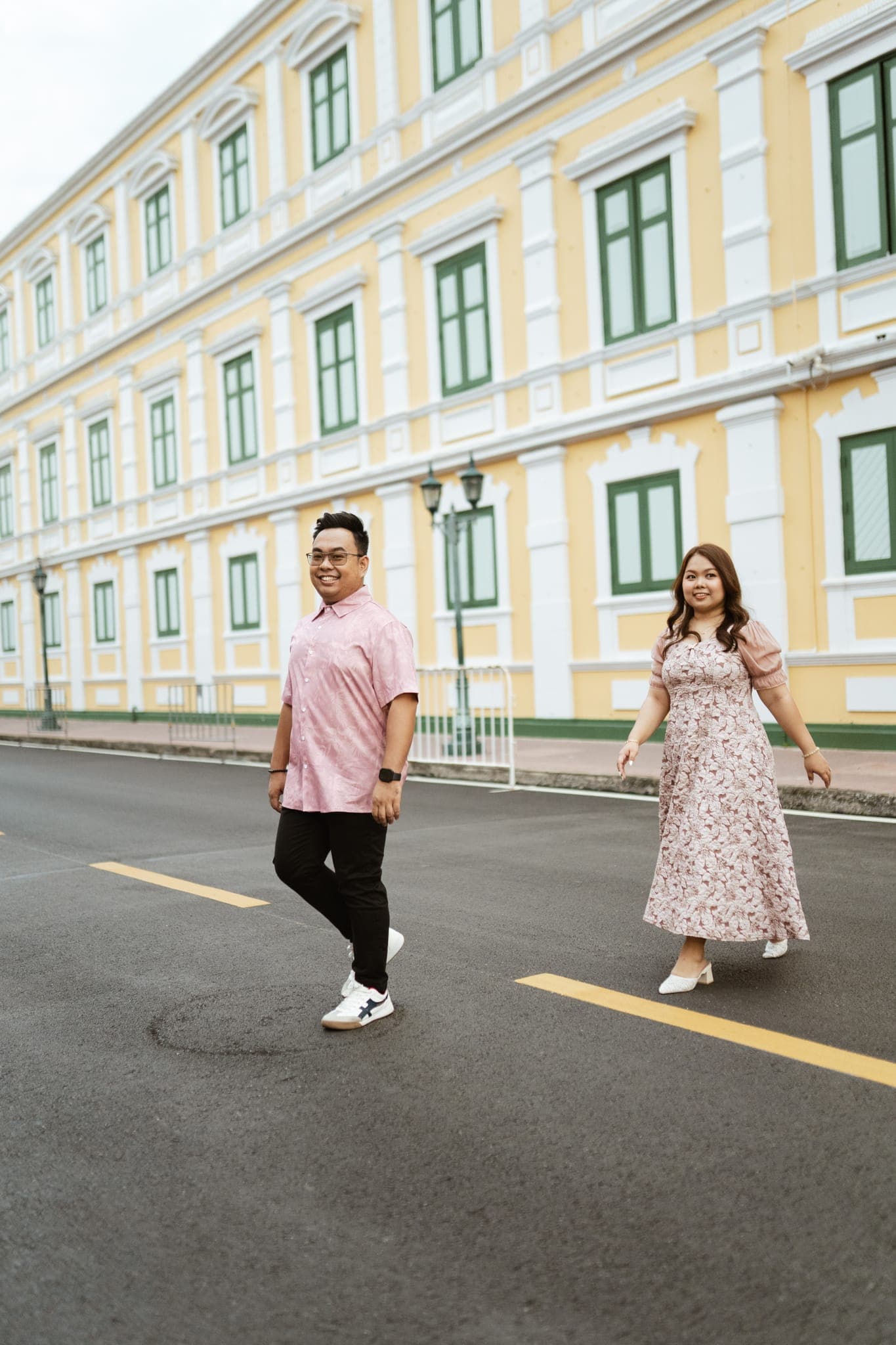 Sam and Angela walking toward each other on a street lined by a long yellow building