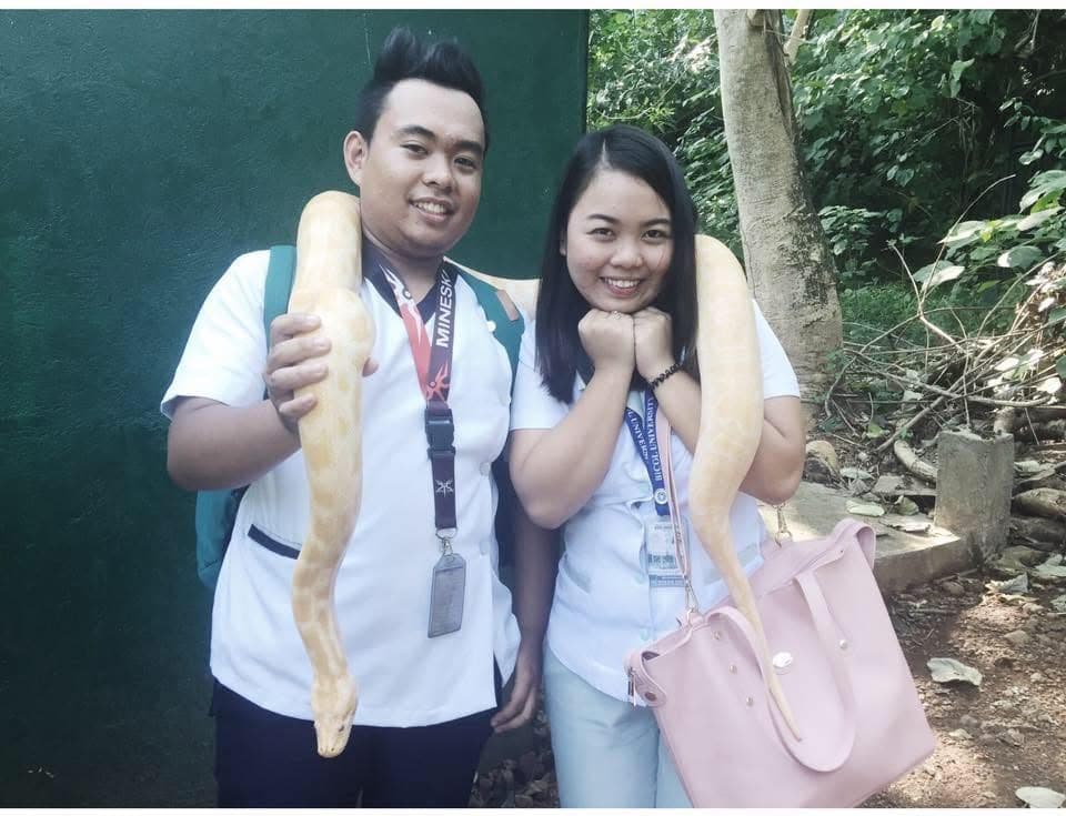 Sam and Angela in school uniforms, each with a pale yellow python draped over their shoulders