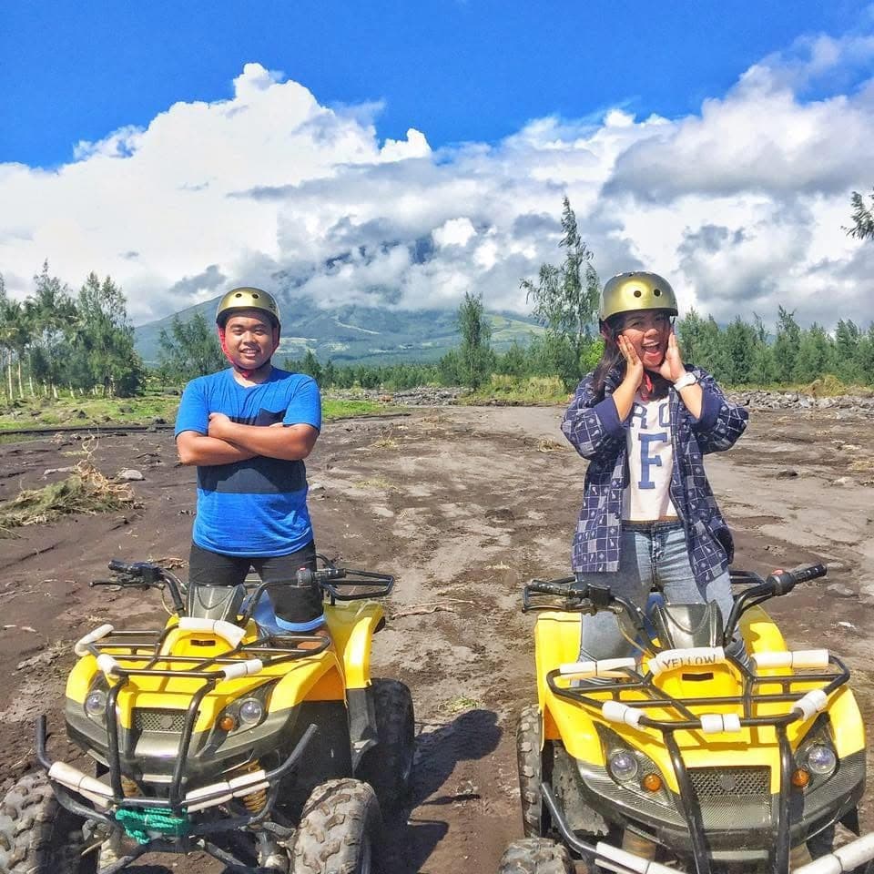 Sam and Angela in helmets beside two yellow ATVs on a rocky volcanic trail