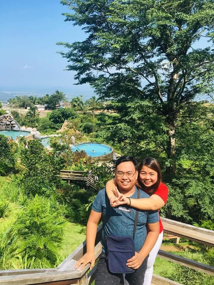Angela hugging Sam from behind at a hillside lookout above a resort pool